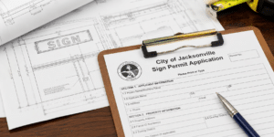 A close-up of a commercial sign permit application and architectural blueprints on a desk.